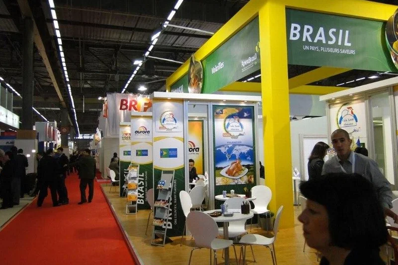 Suasana paviliun stan booth pameran makanan dan minuman F&B berskala internasional dengan konstruksi kanopi overhead kuning berlampu downlight, lantai raised floor laminasi kayu, partisi bilik meeting modular, dan sirkulasi pengunjung di lorong pameran