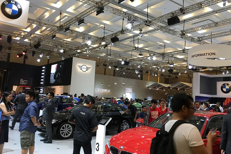 Pengunjung berkeliling di antara booth pameran dengan rigging lampu truss dan mobil display di dalam hall konvensi