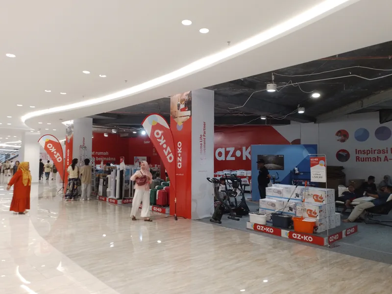 Stand pameran pop-up store dan bazar produk di koridor mall berlantai marmer dengan podium display, backdrop merah, dan antusiasme pengunjung
